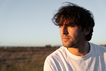 Man with curly hair contemplating outdoors during sunset, feeling peaceful and enjoying nature