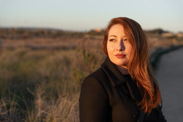 Woman with red hair enjoying autumn sunset, looking away reflecting on nature and tranquility feeling hope