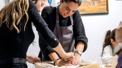 Fototapeta premium In an art studio two beautiful middle-aged artist friends are working on clay shaping at a table