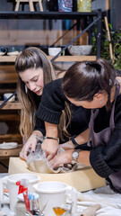 In an art studio two beautiful middle-aged artist friends are working on clay shaping at a table