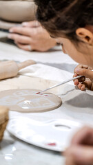 In an art studio during an art event, a young girl child is painting a shape she made from clay