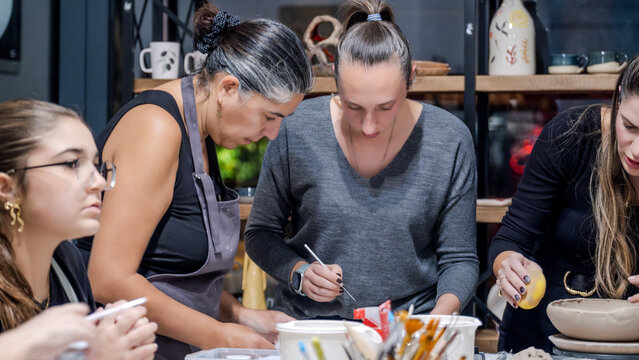 In an art studio during a group art event, a group of women and children are enjoying a creative hobby, learning and having fun as they make shapes out of clay