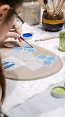 During an art event in a studio, a girl child is painting Christmas ornament shapes she crafted on clay