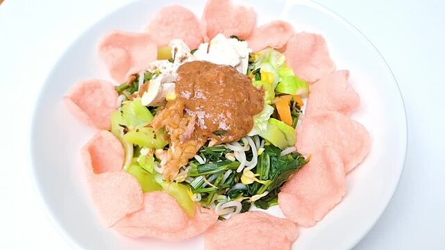 A plate of Indonesian gado-gado vegetables topped with savory peanut sauce and crunchy crackers.