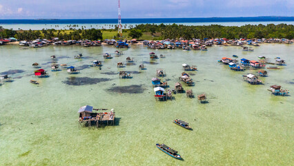 Aerial view of sea gypsy village over clear turquoise waters in Kulapuan Island Semporna, Sabah, Malaysia. Scenic seascape with coral reefs, coastal village, and blue tropical sky.