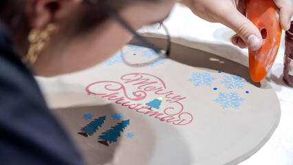 During an art event in a studio, middle age woman is painting Christmas ornament shapes she crafted on clay