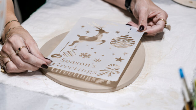 During an art event in a studio, middle age woman is painting Christmas ornament shapes she crafted on clay - Powered by Adobe