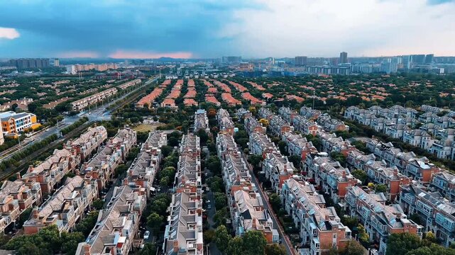 4K aerial drone footage shows a residential neighborhood surrounded by lush greenery and a nearby urban skyline in the distance.