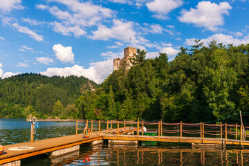 A wooden pier extends into the shimmering waters of czorsztyn lake, with niedzica castle tower...