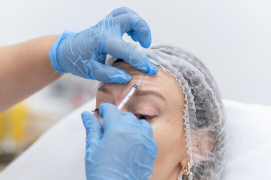 A professional performs botulinum therapy on a client at a well-equipped clinic, focusing on facial wrinkles and skin rejuvenation.