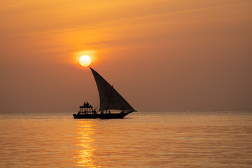 Traditional wooden dhow boat, sails past the setting sun, in the Indian Ocean, Zanzibar, Tanzania