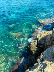 Rocky shoreline meets clear blue waters under bright sunlight in a serene coastal landscape