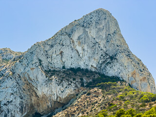 Large rocky mountain with steep cliffs under a clear blue sky during midday