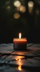 Orange candle with flame glowing sits on burlap on a weathered wooden surface, covered in water droplets on a dark background