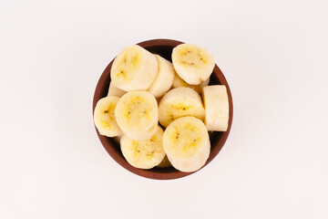 Fresh banana slices overflow a dark wooden bowl providing texture and color contrast from above.