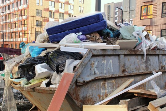 Overfilled dumpster in urban area. Construction debris overflowing a large container. Waste garbage bin with construction materials. Dumpster full of mixed construction and demolition waste