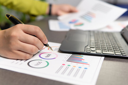 Analyzing financial data through charts and graphs, marketing reports on computer screens and examining paper graphs, financial statistics.