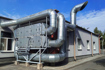 Large-scale industrial ventilation system with metal pipes and a square filter unit. Robust construction and sophisticated air ducts.