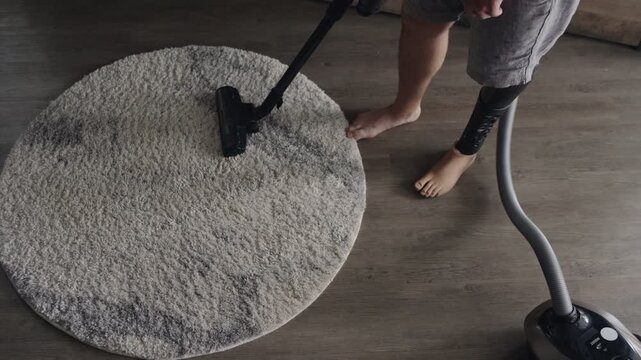 Overhead shot of an amputee vacuuming a living room carpet with a bionic leg, showcasing technology in everyday life.