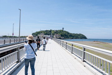 People walking on seaside promenade near island with lighthouse on sunny day at Enoshima, Kamakura,...