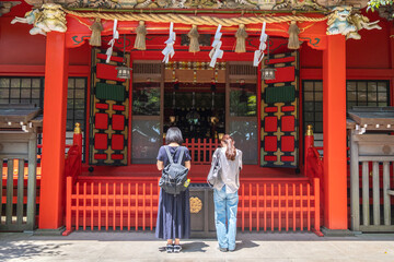 Two women praying at traditional Japanese shrine entrance outdoors at Enoshima, Kamakura, Kanagawa, Japan