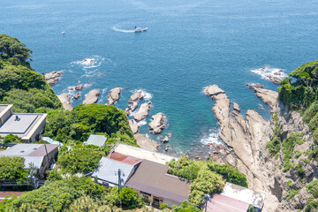 Coastal houses near rocky shoreline with clear blue sea and fishing boat at Enoshima, Kamakura, Kanagawa, Japan