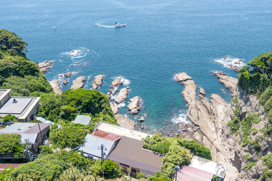 Coastal houses near rocky shoreline with clear blue sea and fishing boat at Enoshima, Kamakura, Kanagawa, Japan
