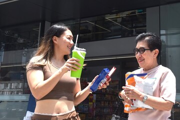 mother and daughter buy cold drink with some snacks and walking in front of convenience store