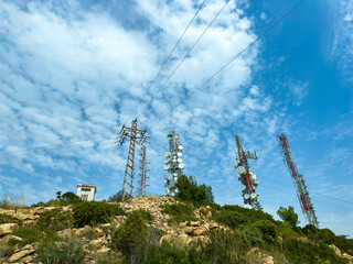 Communication towers and power lines stand tall against a blue sky with scattered clouds, captured...