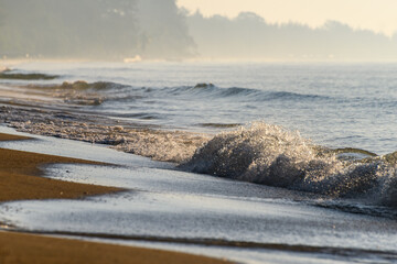 Misty ocean waves breaking on sandy shoreline.