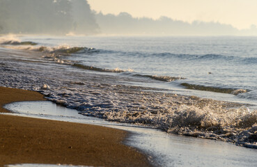 Misty ocean waves breaking on sandy shoreline.