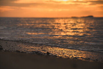 Golden morning light reflecting on ripples along sandy beach.