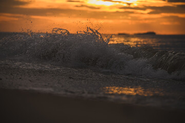 Golden morning light reflecting on ripples along sandy beach.