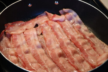 Multiple slices of raw bacon laid out on the frying pan