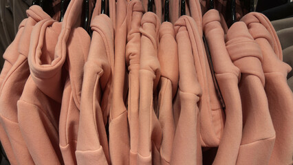 Row of pink hoodies on hangers in clothing store, casual sweatshirts with hoods and drawstrings,...