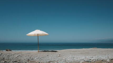 White beach umbrella on a pebble beach with the turquoise ocean in the background