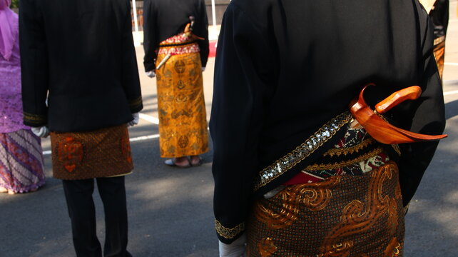 Men wearing traditional keris and batik sarong stand in formation during a cultural celebration, showcasing Indonesian heritage and pride.