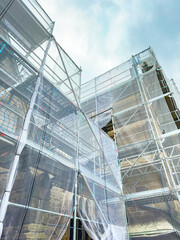 Renovation work on a historic building under scaffolding during a cloudy day with a hint of sunlight shining through