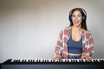 Portrait of young woman smiling while playing digital piano with headphones indoors, music...