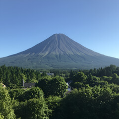 A majestic conical mountain, possibly a volcano, rises dramatically above a lush green forest under a clear blue sky, showcasing serene natural beauty.