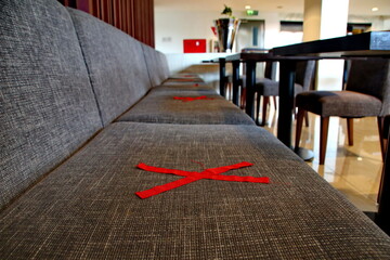Empty sofa in a restaurant marked with red tape for social distancing during the coronavirus pandemic, creating a sense of isolation and caution.