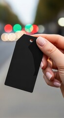 Hand holding a blank black tag against a blurred urban background with colorful bokeh lights, showcasing the potential for branding and customization in a modern retail environment