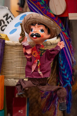 Obraz premium A small, colorful toy figure of a man dressed in a sombrero and red shirt is suspended from a basket. Historic center of Queretaro City, decorations and traditions to celebrate Mexico's Independence D
