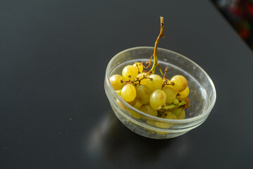 White grapes with brown spots as proof that they are organic and unsprayed in a glass bowl showing refrigerator stains on a dark table