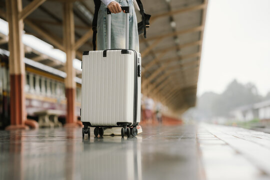 Stylish young woman traveling at train station with suitcase, traveling alone on vacation or business trip, enjoying summer city adventure.