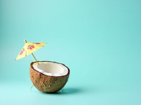 Tropical vacation and summer holiday concept with a fresh coconut half and cocktail umbrella on a turquoise background.