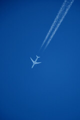 Airplane in the blue sky with contrail, closeup of photo. Airplane in the blue sky with white trace of a plane.