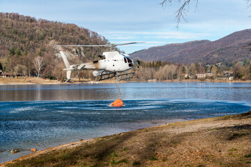 Firefighting helicopter dropping water on mountain fire above Lake Ghirla in Valganna, Province of Varese, Italy