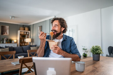 Happy man eating takeout noodles working from home