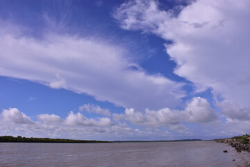 Obraz premium Scenic wide-angle view of the Bakkhali River in Cox’s Bazar, Bangladesh, with flowing water under a dramatic blue sky filled with white clouds. A natural landscape of river and sky.